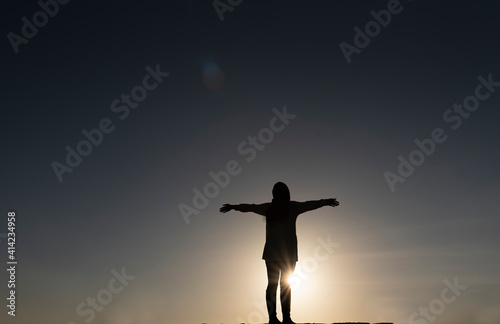 Silhouette of a young dancing woman with long wavy hair in the mountains in the backdrop of the setting sun 