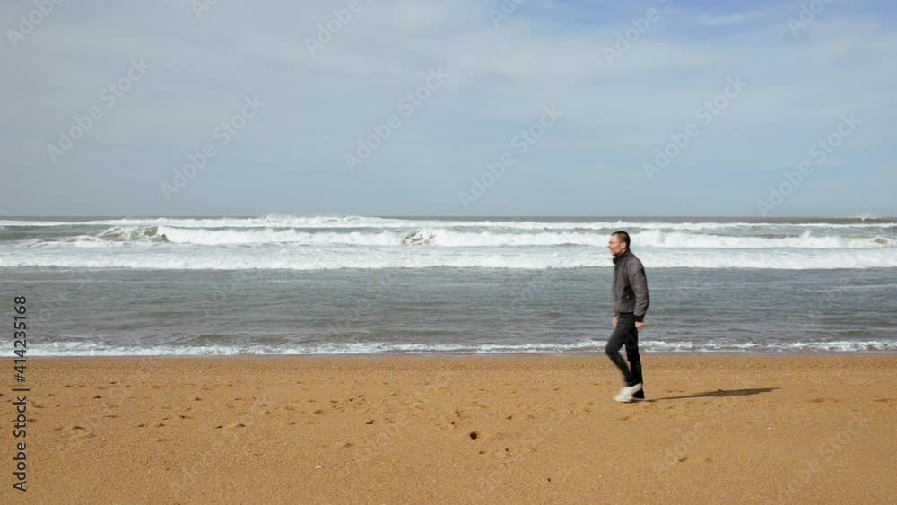 Man walking along the Atlantic ocean on sandy beach, static shot Man walking along the Atlantic ocean on sandy beach, static shot