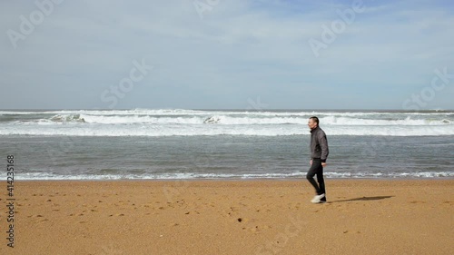 Man walking along the Atlantic ocean on sandy beach, static shot