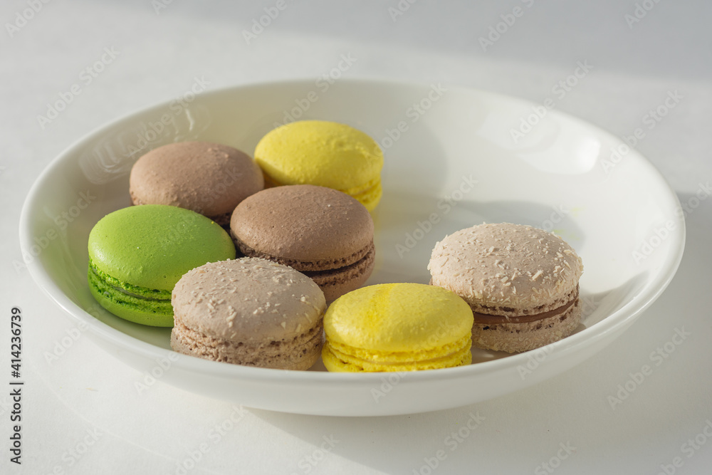 Colorful macaroons on a white plate. exquisite French delicacy. horizontal photo. Close-up, top view. green, yellow, brown cookies. taste of apple, chocolate and lemon. Colorful macaroons on a white plate. exquisite French delicacy. horizontal photo. Close-up, top view. green, yellow, brown cookies. taste of apple, chocolate and lemon.