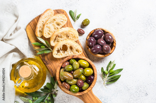 Olives in wooden bowls, ciabatta bread and olive oil on white background. Top view with copy space.