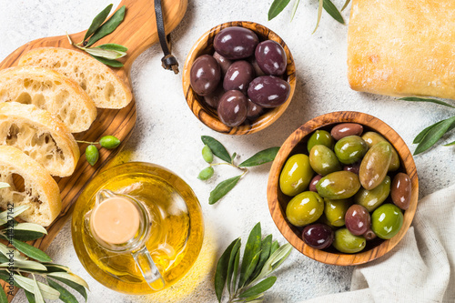 Olives in wooden bowls, ciabatta and olive oil on white background. Top view with copy space.