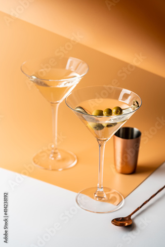 Cocktail vodka martini with green olives on orange background with bright beautiful shadows