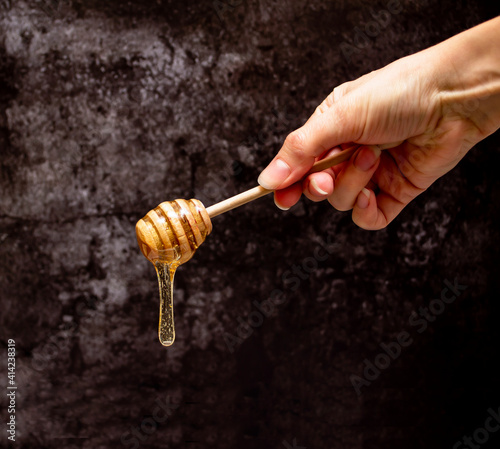 Wooden honey spoon in hand with hanging drop on dark background with copy space