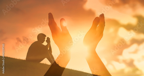 Young man praying reaching out to the sunset sky feeling warm rays of sunshine.  photo