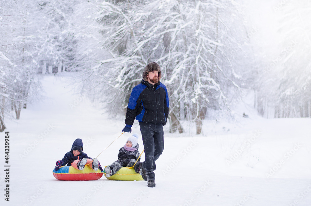 dad and two girls. a man carries two children on an inflatable sled in a winter forest