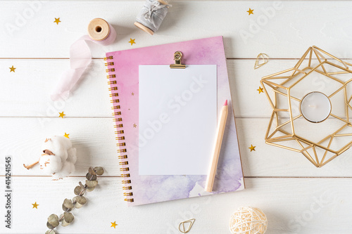 Top view of white working table background with blank paper notebook, nature cotton. Flat lay still life candle, golden paper binder clips. Notepad and pen. Desktop mockup, workspace, stationery.