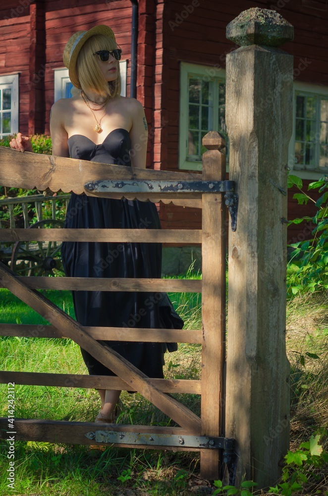 beautiful woman in a summer park stands at the  vintage wooden gate 