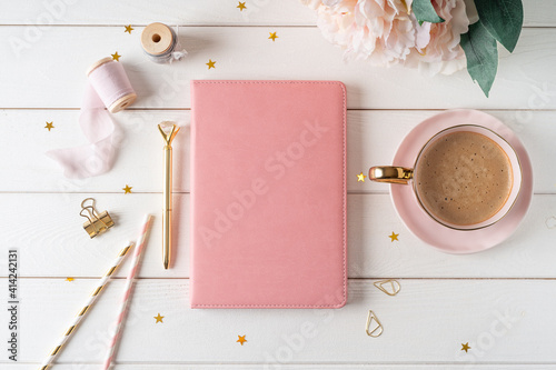 Top view of white working table background with blank paper notebook, cup of coffee. Flat lay peonies flowers, golden paper binder clips. Notepad and pen. Desktop mockup, workspace, stationery.