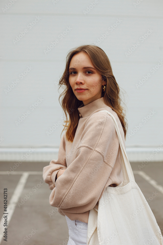 a young girl with wavy hair stands with a white eco bag near white wall on the the parking a young girl with wavy hair stands with a white eco bag near white wall on the the parking