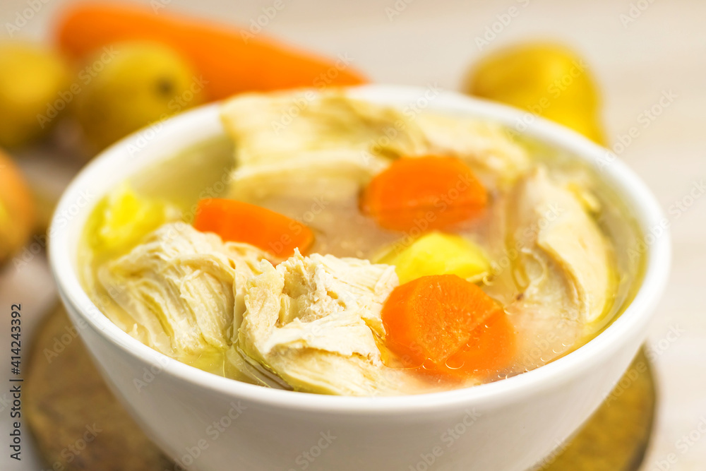 Chicken Soup stew broth and vegetables in white bowl on old rustic wooden cutting board Chicken Soup stew broth and vegetables in white bowl on old rustic wooden cutting board