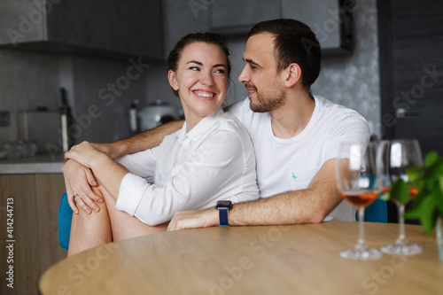 young couple in love have fun each other in the kitchen. happy smiling man and woman hugging  at home indoor. romantic date . happy family sitting on the kitchen with two glass of white wine 