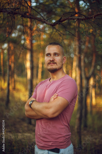 Fototapeta Naklejka Na Ścianę i Meble -  sporty guy with a beard dreamily looking to the side with his arms crossed in the forest at sunset