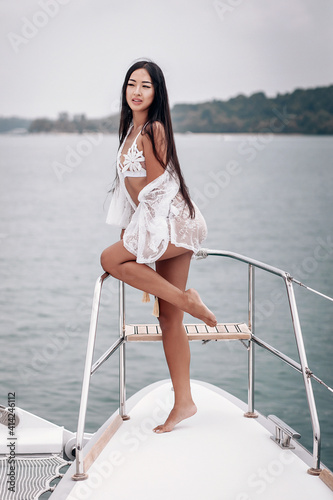 Sexual young lady with raised leg, wearing a white bikini, is posing on the yacht, portrait