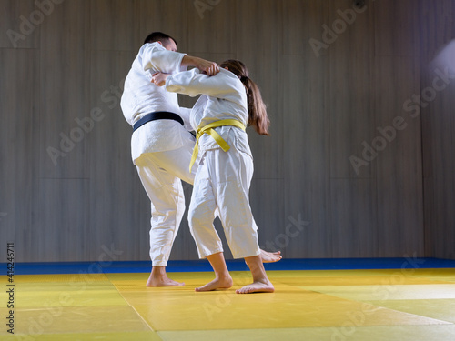 Black belt judoka demonstrating o soto gari technique on young female student
