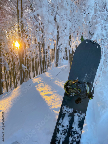 VERTICAL: Sunset illuminates the forest and a snowboard stuck in fresh snow.