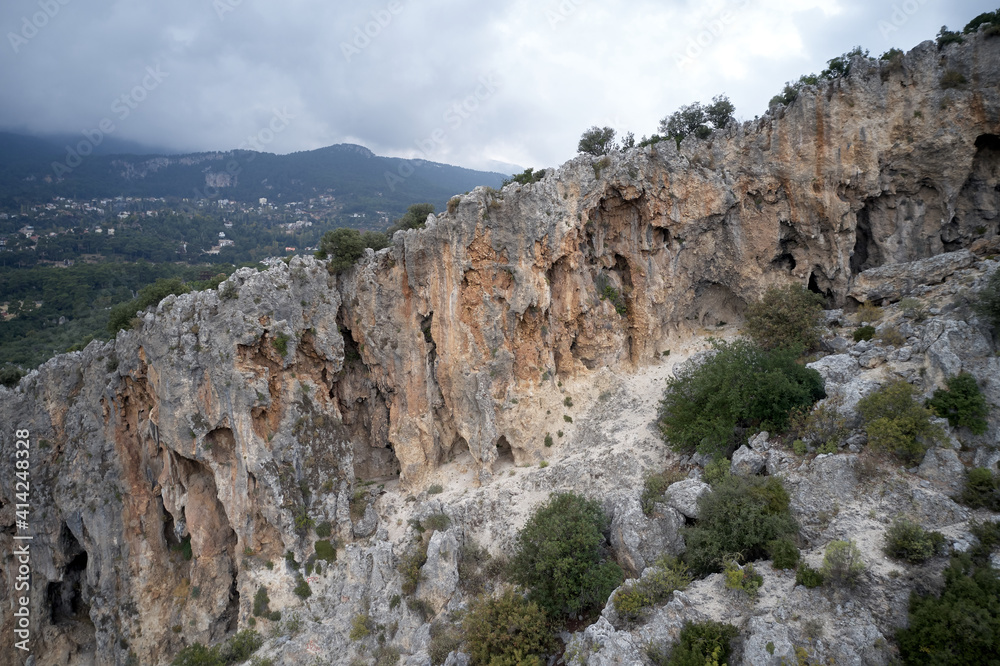 Naklejka premium Rocky mountain cliff and green trees. Cloudy sky in the background.