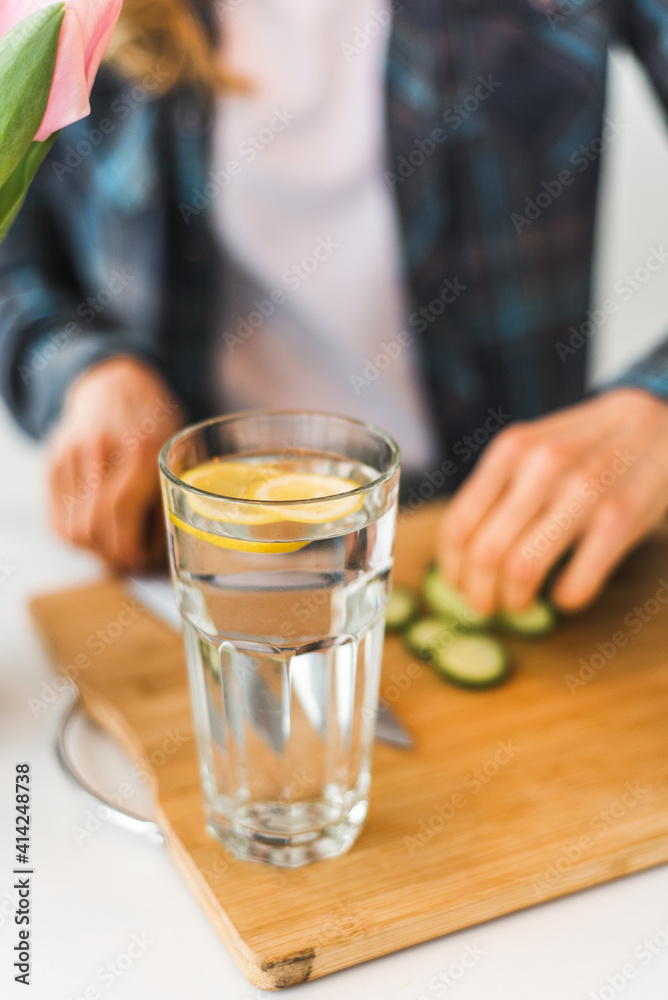 The girl prepares homemade lemonade with cucumber and lemon in the kitchen on a white table. Detox and diet food
