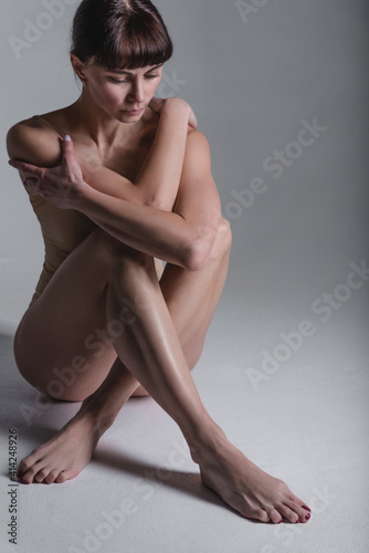 Attractive, slim, adult woman in a beige swimsuit on a gray background in the studio. The concept of a beautiful figure, body positive, healthy lifestyle