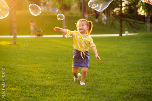 Happy little girl 4-5 years old plays with soap bubbles in the summer in the park. Children s lifestyle.