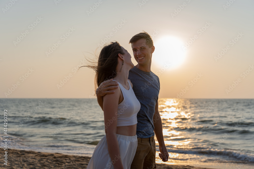 Young happy couple walking on the beach during sunset