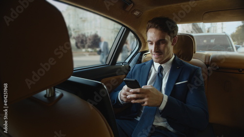 Happy male professional writing message on smartphone in business car. © stockbusters