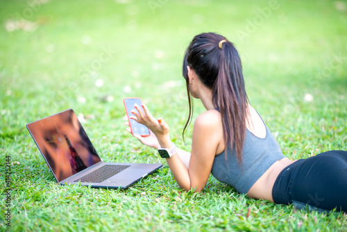 Beautiful asian girl lying down on the grass using laptop and smartphone