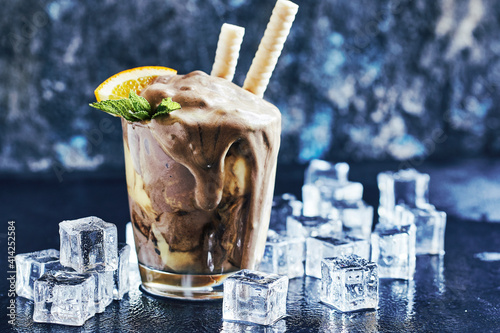 Orange Soda Creamsicle Ice Cream Float in glass decorated with piece of orange, straws and leaves on mint, surrounded by ice cubes on stone table backdrop photo