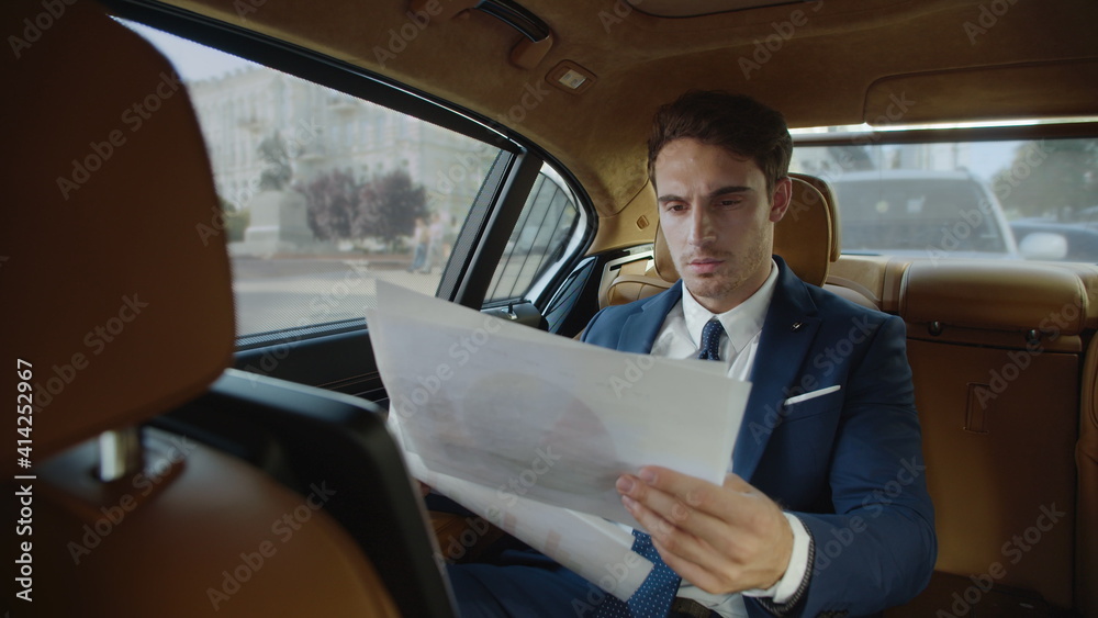 Elegant businessman reviewing statistics in paperwork in modern car.