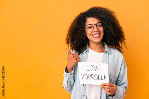 Young african american curly woman holding a love yourself placard smiling and raising thumb up photo