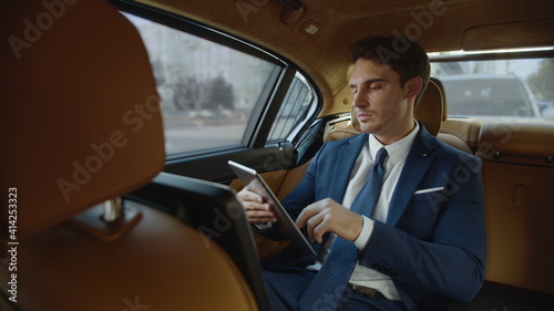 Focused male professional reading documents on digital tablet in modern car. © stockbusters