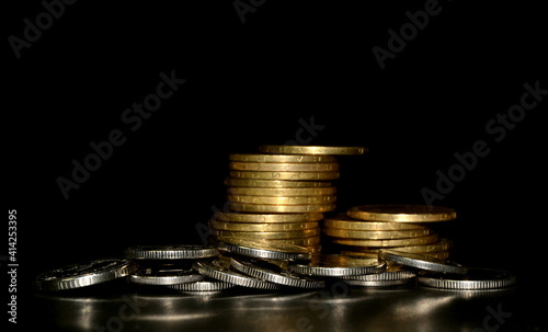 Stack of golden coins and heap of silver coins on a black background