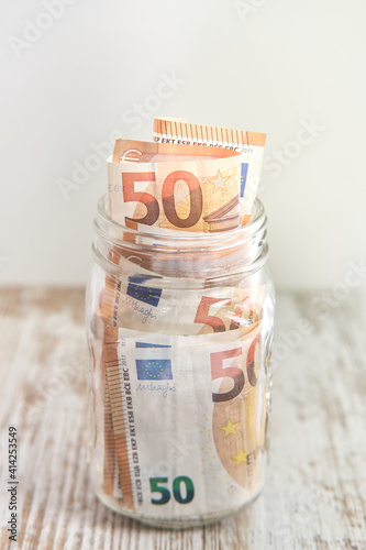Fifty euro banknotes in a glass jar on rustic wooden table background with copy space. Savings concept.