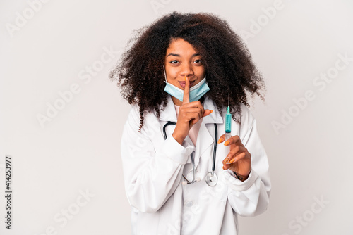 Young african american curly doctor woman holding a syringe keeping a secret or asking for silence. © Asier