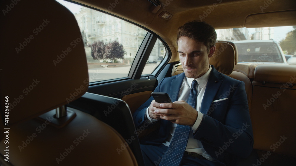 Aggressive businessman writing angry message on mobile phone in modern car.