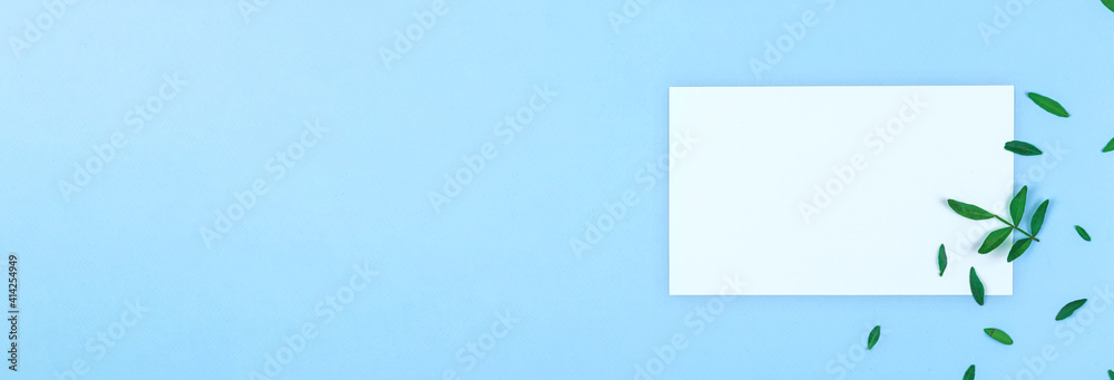Mockup with blank paper and flat lay blue pastel color background, natural green leaves and branches, banner and copy space Mockup with blank paper and flat lay blue pastel color background, natural green leaves and branches, banner and copy space