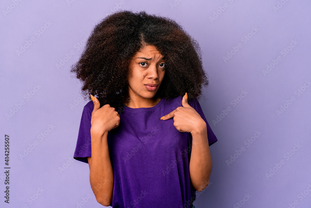 Young african american curly woman isolated on purple background surprised pointing with finger, smiling broadly. Young african american curly woman isolated on purple background surprised pointing with finger, smiling broadly.