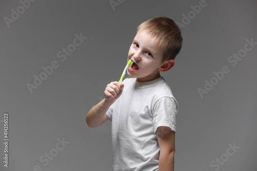 Happy child kid boy brushing teeth with toothbrush on gray background. Health care, dental hygiene. Mockup, copy space photo