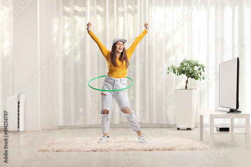 Fototapeta Naklejka Na Ścianę i Meble -  Young woman spinning a hula hoop at home in a living room