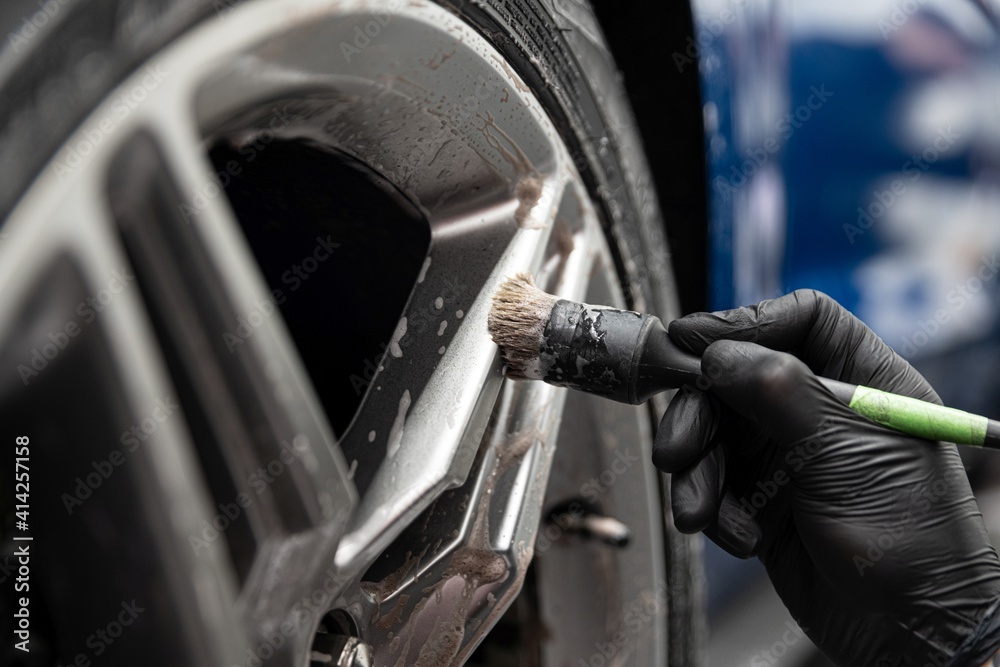 Car detailing studio worker cleaning car wheel with brush
