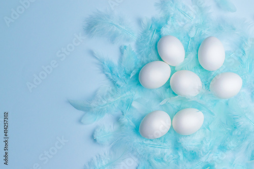 White Easter eggs and decorated with feather on a blue background. Space for text. Top view