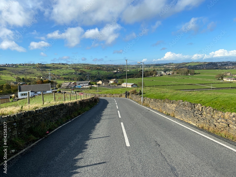 Fototapeta premium View down, Back Lane, with dry stone walls, fields, farms and distant hills near, Bradford, Yorkshire, UK