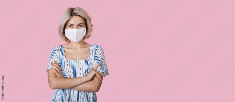 Adorable young woman with blonde hair and medical mask on face is smiling at camera and advertising something near pink studio free space Adorable young woman with blonde hair and medical mask on face is smiling at camera and advertising something near pink studio free space