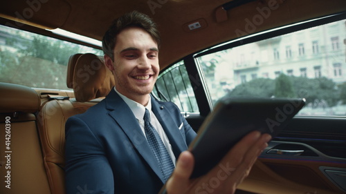 Happy male professional reading messages on tablet computer in business car. © stockbusters