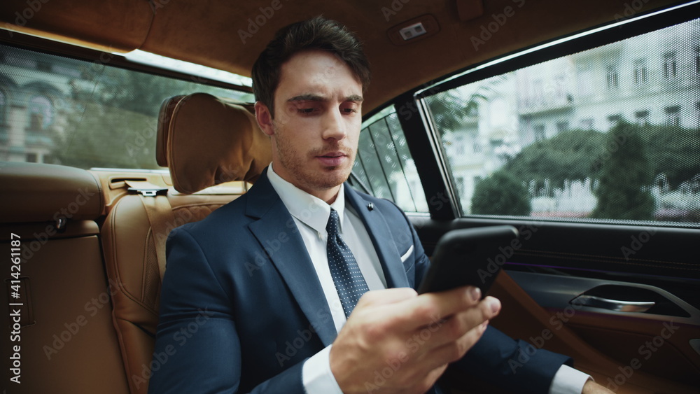 Upset male professional reading bad news on smartphone in salon of business car.