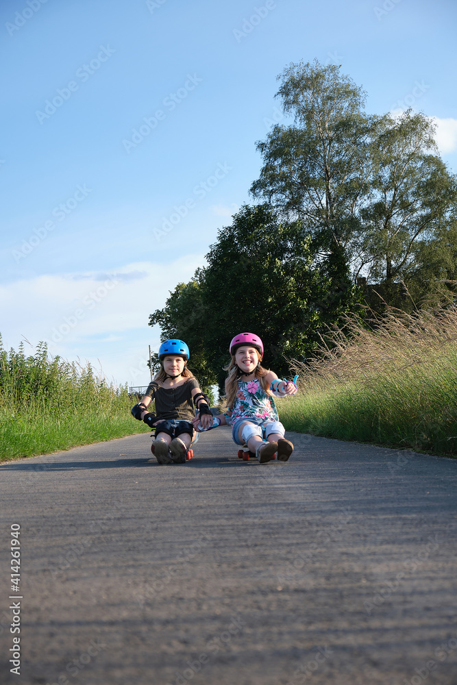 identical twin sisters having fun with their scateboards on a sunny summer day. Two active girls and their hobby.