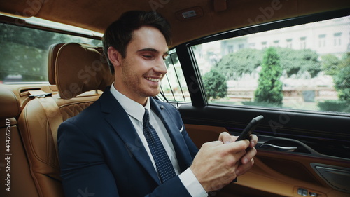Joyful businessman writing message on smartphone in luxury car. © stockbusters
