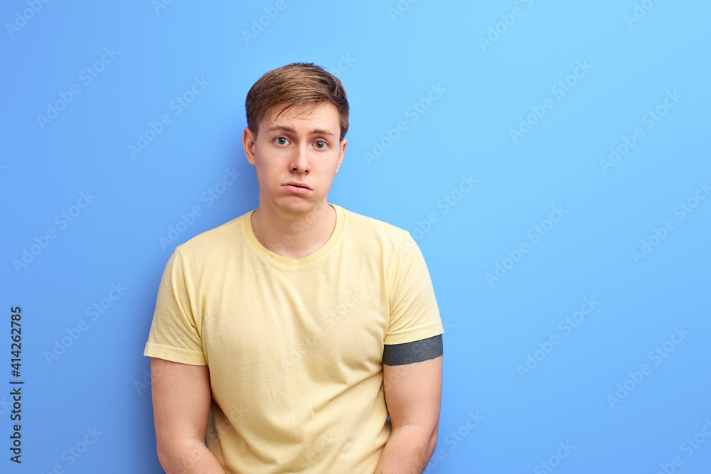 upset man standing and looking at camera with dissatisfied sadness face, indoor studio shot, isolated on blue background, portrait upset man standing and looking at camera with dissatisfied sadness face, indoor studio shot, isolated on blue background, portrait