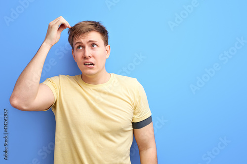 man looks away and thinks with a doubtful face, try to remember something, isolated on blue background. studio portrait of caucasian male in casual t-shir looking up