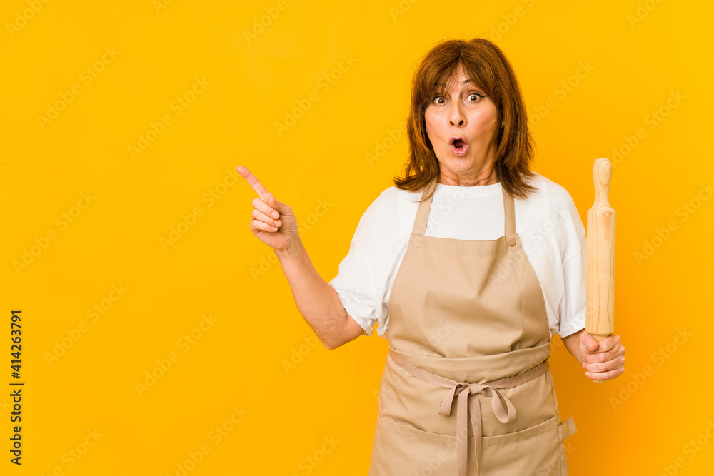 Middle age caucasian cook woman holding a roller isolated pointing to the side